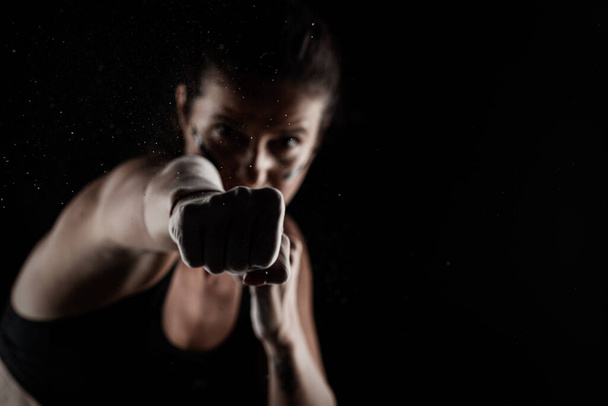 Kickboxer kirl with magnesium powder on her hands punching with dust visible. - Fotó, kép
