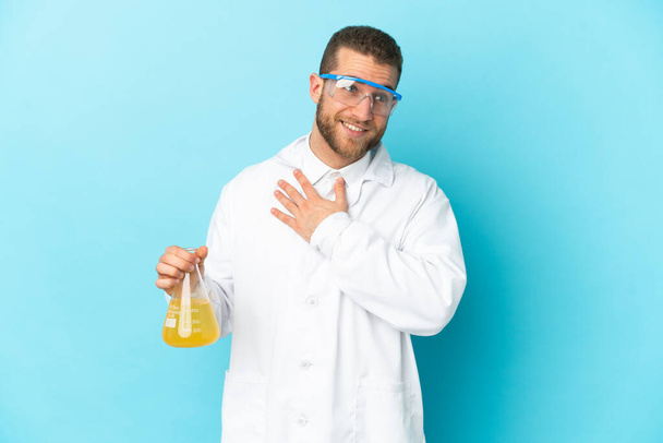 Young caucasian scientific man isolated on blue background looking up while smiling - Foto, Bild