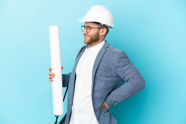 Young architect man with helmet and holding blueprints over isolated background suffering from backache for having made an effort - Φωτογραφία, εικόνα