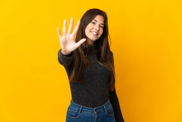Adolescente brasileña aislada sobre fondo amarillo contando cinco con los dedos - Foto, imagen