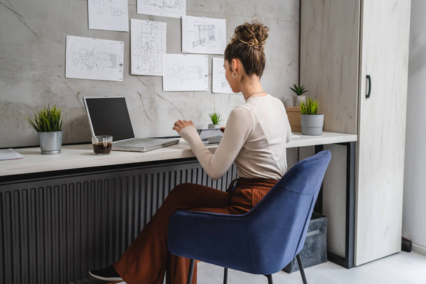 Genç beyaz bir kadın ofis masasında oturmuş laptopta çalışırken dinlenen belgeleri inceliyor gerçek insanlar uzay mühendisi kadın projesini kopyalıyor. - Fotoğraf, Görsel