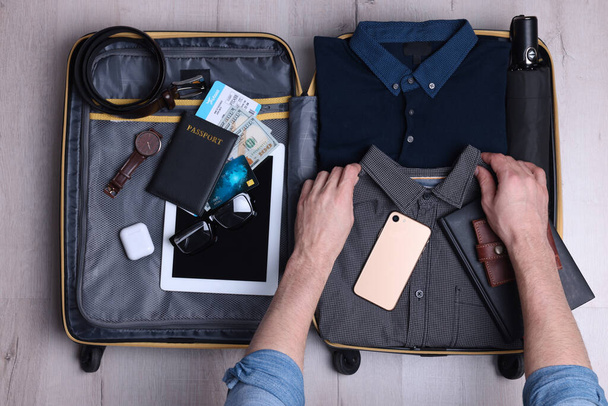 Man packing suitcase for business trip on wooden floor, top view - 写真・画像