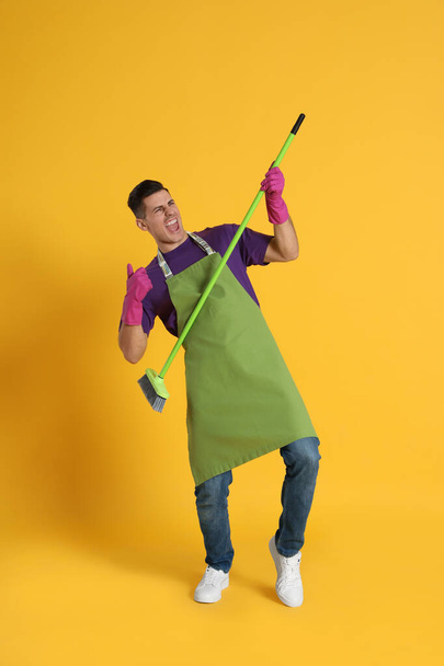 Man with green broom having fun on orange background - Zdjęcie, obraz