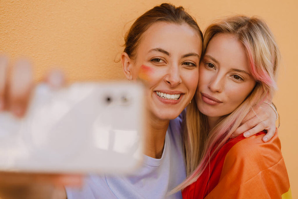 Young lesbian couple smiling and taking selfie photo over yellow wall - Fotoğraf, Görsel