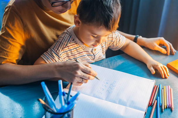 Matka uczy matematyki numer jej syna w domu. Mama i chłopiec ręka w rękę pisząc numery, świetny projekt do wszelkich celów. - Zdjęcie, obraz