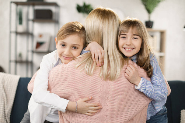Happy affectionate family mom and two cute little kids embrace and looking at the camera - Фото, зображення