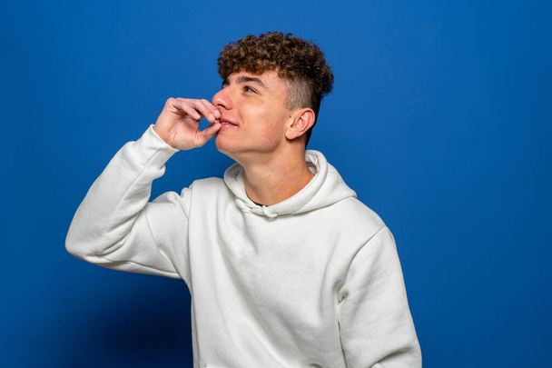 Smiling caucasian young man with hand on mouth looking interested aside at copy space isolated on blue background thinking of shopping opportunities, planning purchases or dreaming concept. - Photo, Image
