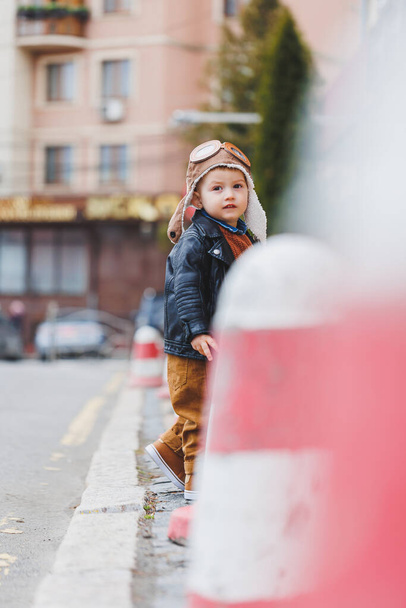 Stylish boy 3 years old in a leather jacket and brown trousers walks on the street. Modern child. Children's fashion. Happy child - Fotó, kép