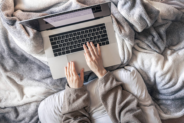 Uma mulher trabalhando em um laptop enquanto deitada na cama, vista superior. - Foto, Imagem