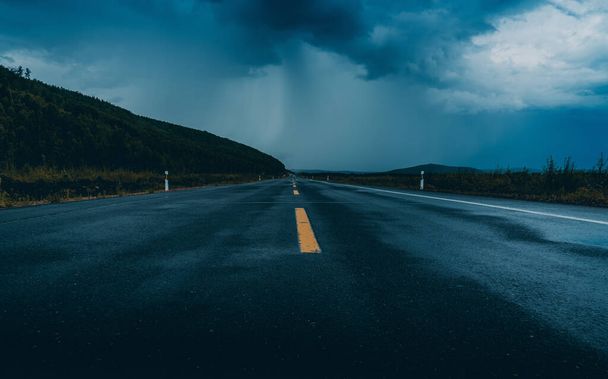 雨の後、暗い背景に山と暗い雲と高速道路. - 写真・画像