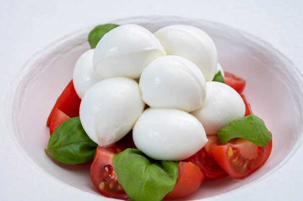 Итальянская еда, вкусный салат капрезе с красными помидорами черри, белый сыр моцарелла и зеленые листья базилика - Фото, изображение