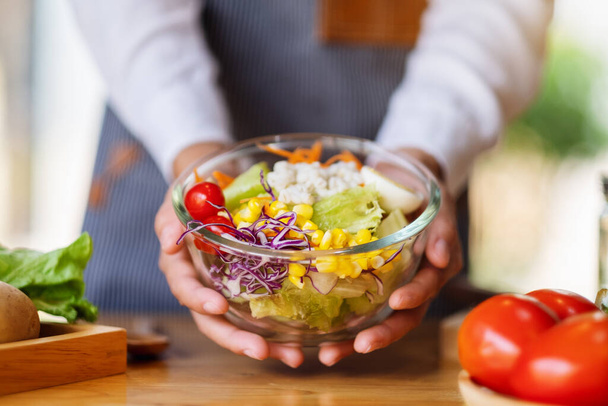 Lähikuva kuva naiskokki ruoanlaitto ja pitämällä kulhoon tuoreita sekoitettuja vihanneksia salaattia keittiössä - Valokuva, kuva
