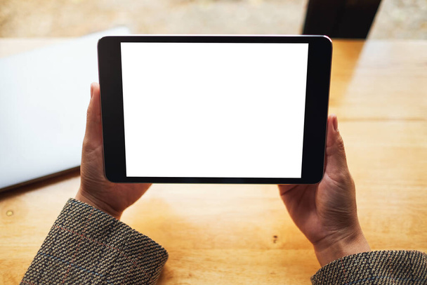 Image maquette d'une femme assise et tenant une tablette noire pc avec écran blanc vierge de bureau avec ordinateur portable sur la table  - Photo, image