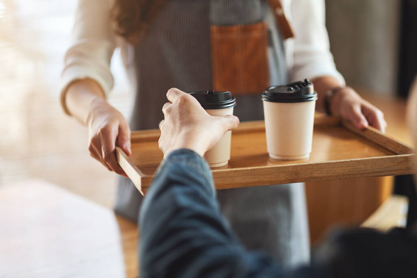 Una camarera sosteniendo y sirviendo tazas de café caliente al cliente en la cafetería - Foto, imagen