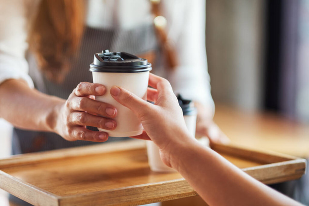 Офіціантка тримає і подає паперові чашки гарячої кави клієнту в кафе
 - Фото, зображення
