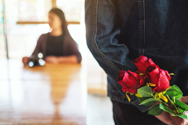 Мужчина, который держит и прячет букет красных роз на спине, чтобы удивить девушку - Фото, изображение