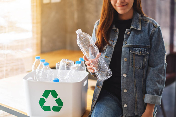 Красива азіатська жінка тримає і збирає пластикові пляшки для переробки сміття в смітник вдома
 - Фото, зображення