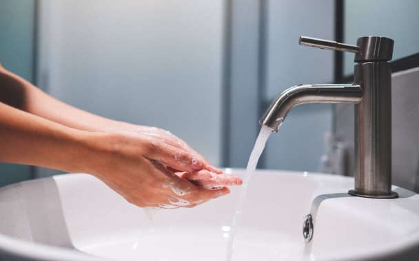 Mujer limpiando y lavando las manos con jabón debajo del grifo en el baño - Foto, imagen