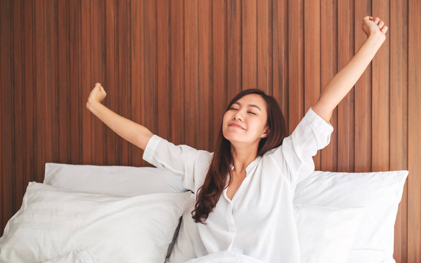 Güzel bir Asyalı kadın, sabah kalktıktan sonra evdeki beyaz, rahat bir yatakta esneme hareketleri yapar. - Fotoğraf, Görsel