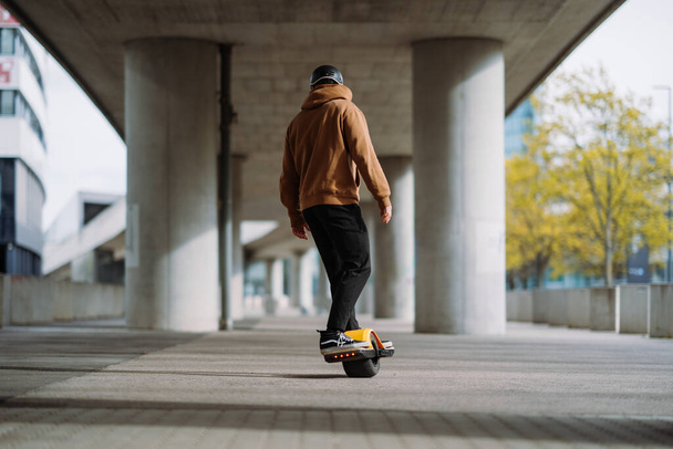 Young man in a helmet rides an electric skateboard. Onewheel rider in an urban background.  - Photo, Image