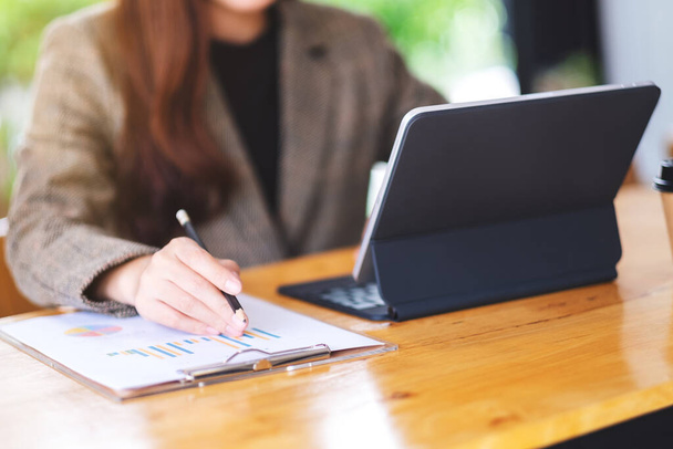 Immagine ravvicinata di una donna d'affari che lavora e utilizza tablet digitale come computer con documento finanziario sul tavolo - Foto, immagini