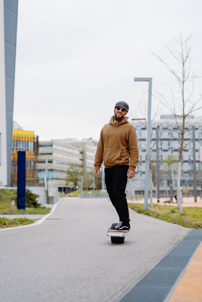 Jongeman met een helm rijdt op een elektrisch skateboard. Onewheel rider in een stedelijke achtergrond. kopieer ruimte verticaal - Foto, afbeelding