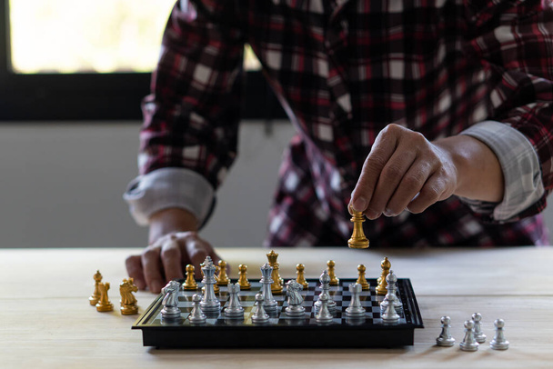 hand houden schaken kan worden geïnterpreteerd in de planning van de concurrentie in het bedrijfsleven Een hoek van het schaakbord in focus, op een houten tafel. - Foto, afbeelding