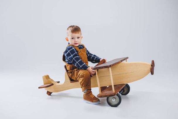 Трехлетний мальчик в клетчатой рубашке сидит на большом деревянном самолете. Детские экологичные игрушки из дерева - Фото, изображение