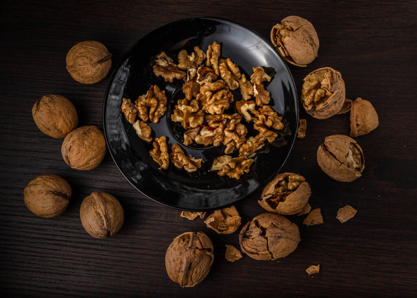 Nuts. Walnut kernels and whole walnuts. Walnuts organic in a black bowl with a woman's hand spoils Walnut with yelow metal nutcraker on a dark wood background. Top view. Walnut healthy - Photo, Image