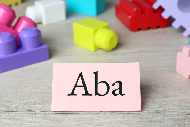 Paper sheet with abbreviation ABA (Applied behavior analysis) and colorful wooden blocks on white table, closeup - Foto, Imagem