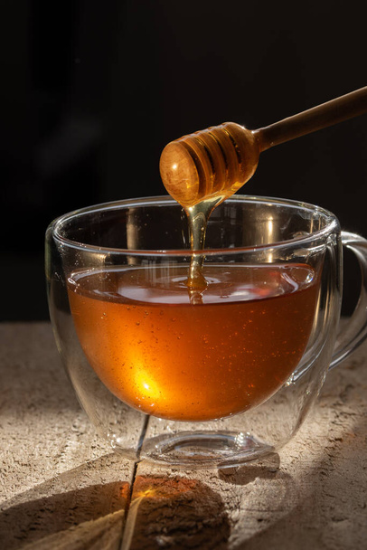 βάζο μελιού σε ξύλινο τραπέζι και σκούρα backgroun, μέλι που στάζει από μέλι dipper - Φωτογραφία, εικόνα