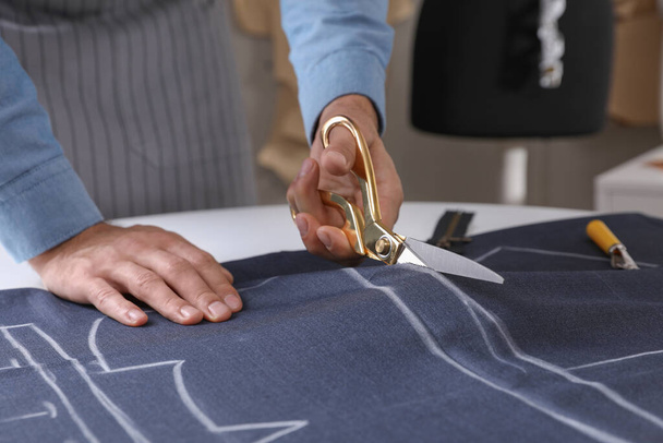 Tailor cutting fabric with scissors at table in atelier, closeup - Valokuva, kuva