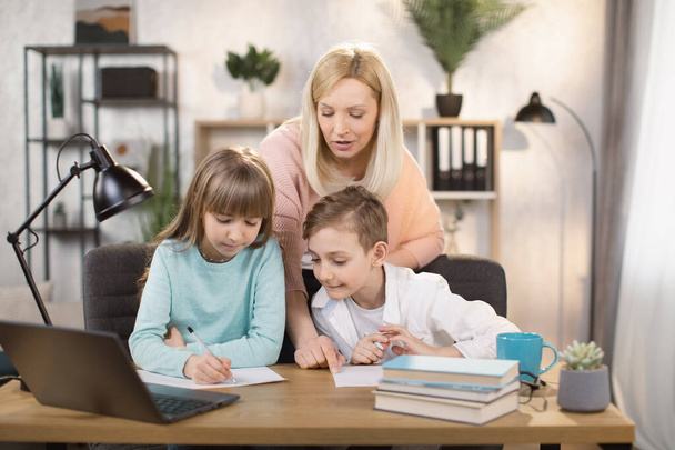 Mother teach young son and daughter homework, using digital laptop at home. - Fotó, kép