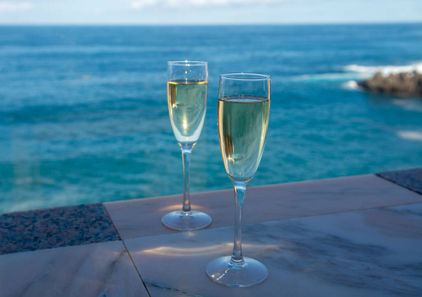 Πρωτοχρονιά γιορτή με δύο ποτήρια σαμπάνια ή ισπανική cava αφρώδη οίνο και θέα στα γαλάζια νερά του Ατλαντικού Ωκεανού, Κανάρια νησιά, χειμερινοί τουρίστες προορισμού - Φωτογραφία, εικόνα