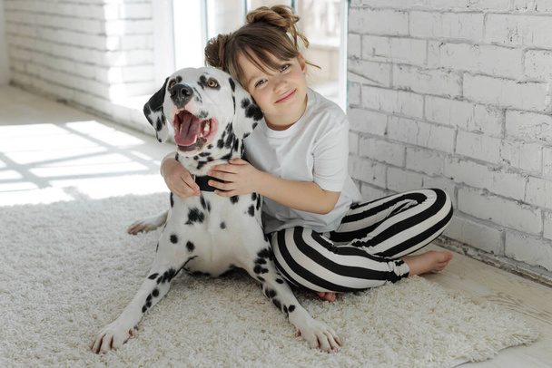 Un niño con un perro. Una chica feliz yace en una alfombra con un perro dálmata. - Foto, Imagen