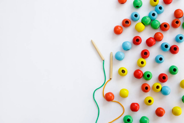 Children development, coordination and cognitive skills concept - toy for motor skills development - colorful wooden beads, lace and needle over white background with copy space - Photo, Image