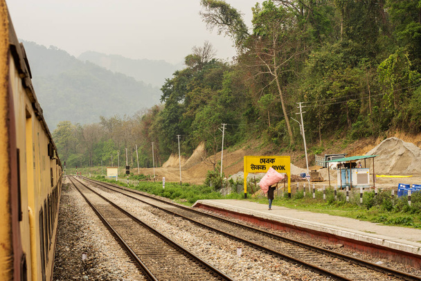5 de abril de 2022, Shevok, Bengala Ocidental, Índia: Um trem amarelo da Indian Railway acabou de chegar à Estação Shevok e poucos passageiros caminhando na plataforma. Montanhas em segundo plano com foco seletivo. - Foto, Imagem