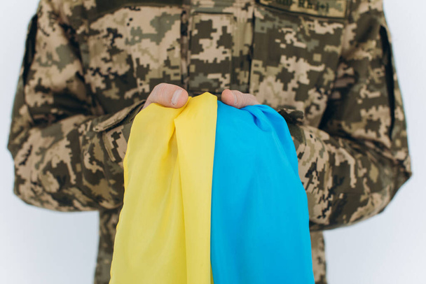Ukrajinský patriot voják ve vojenské uniformě drží žlutou a modrou vlajku na bílém pozadí - Fotografie, Obrázek