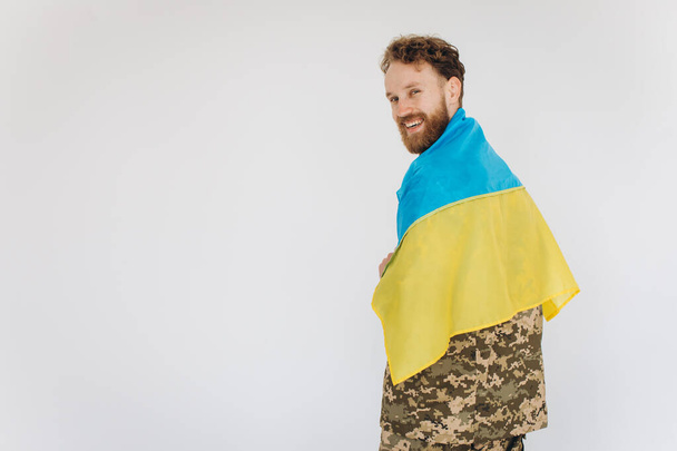 Happy Ukrainian patriot soldier in military uniform holding a yellow and blue flag on a white background - Foto, immagini