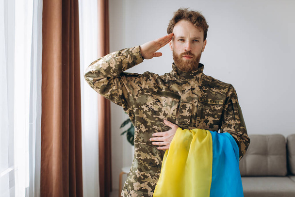 Portret van een Oekraïense soldaat in militair uniform met een gele en blauwe vlag ter ere van - Foto, afbeelding