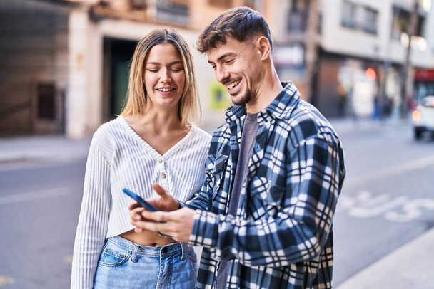 若い男と女のカップル笑顔自信を持って使用してスマートフォンでストリート - 写真・画像
