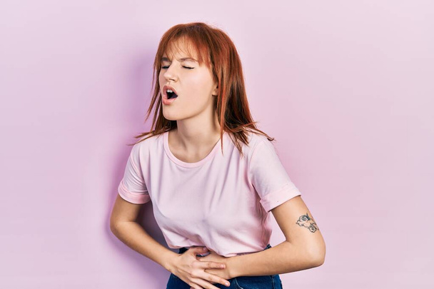 Redhead young woman wearing casual pink t shirt with hand on stomach because nausea, painful disease feeling unwell. ache concept.  - Zdjęcie, obraz
