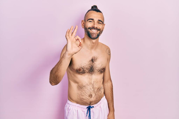 Young hispanic man shirtless wearing swimsuit smiling positive doing ok sign with hand and fingers. successful expression.  - Foto, Imagen