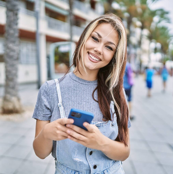 Jeune fille caucasienne souriant heureux en utilisant un smartphone à la ville. - Photo, image