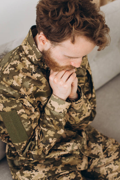 Portrait of emotional young bearded Ukrainian patriot soldier in military uniform sitting on the office sofa - Photo, Image