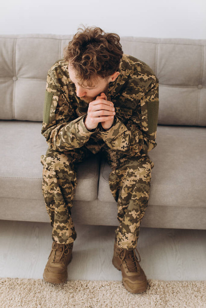 Πορτρέτο της συναισθηματικής νεαρός γενειοφόρος Ουκρανός πατριώτης στρατιώτης με στρατιωτική στολή κάθεται στον καναπέ του γραφείου - Φωτογραφία, εικόνα