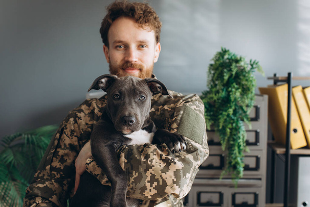 Retrato de un soldado ucraniano y su fiel amigo el perro Amstaff en la oficina - Foto, Imagen