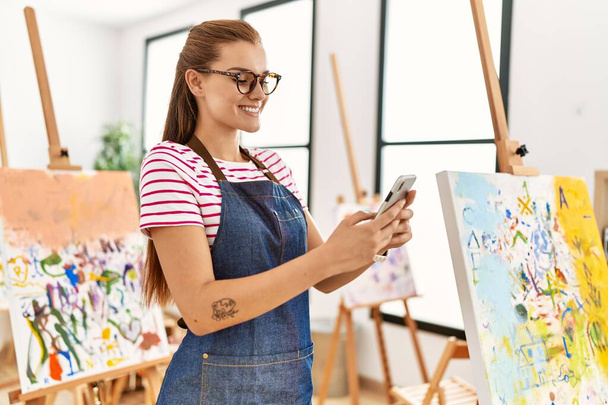 Jeune femme souriant confiant en utilisant smartphone au studio d'art - Photo, image