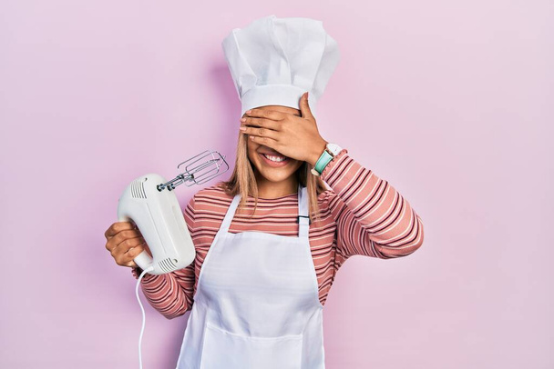 Beautiful hispanic woman holding pastry blender electric mixer smiling and laughing with hand on face covering eyes for surprise. blind concept.  - Φωτογραφία, εικόνα