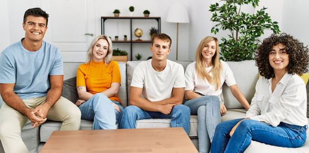 Ryhmä nuoria ystäviä hymyilee onnellinen istuu sohvalla kotona. - Valokuva, kuva